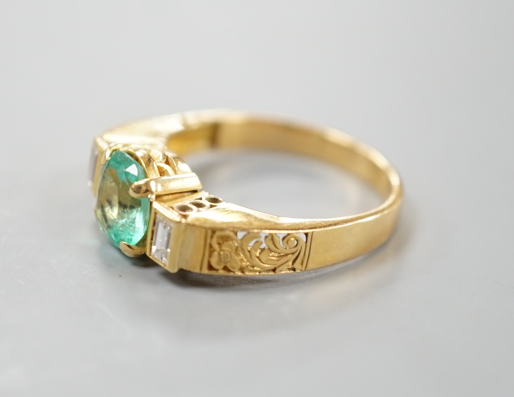 A modern yellow metal, round cut emerald and two stone baguette cut diamond set dress ring, with pierced shoulders, size Q/R, gross 5.5 grams.